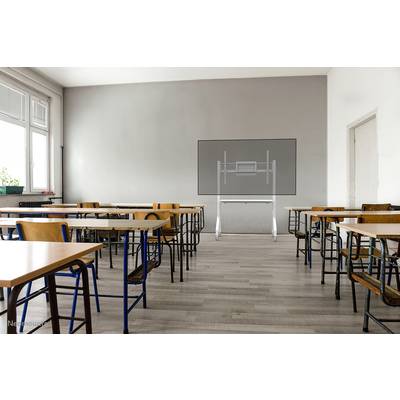 Ein leeres Klassenzimmer mit Tischen und Stühlen, Blick auf eine Wand mit digitalem Whiteboard, Tageslicht von einem großen Fenster.