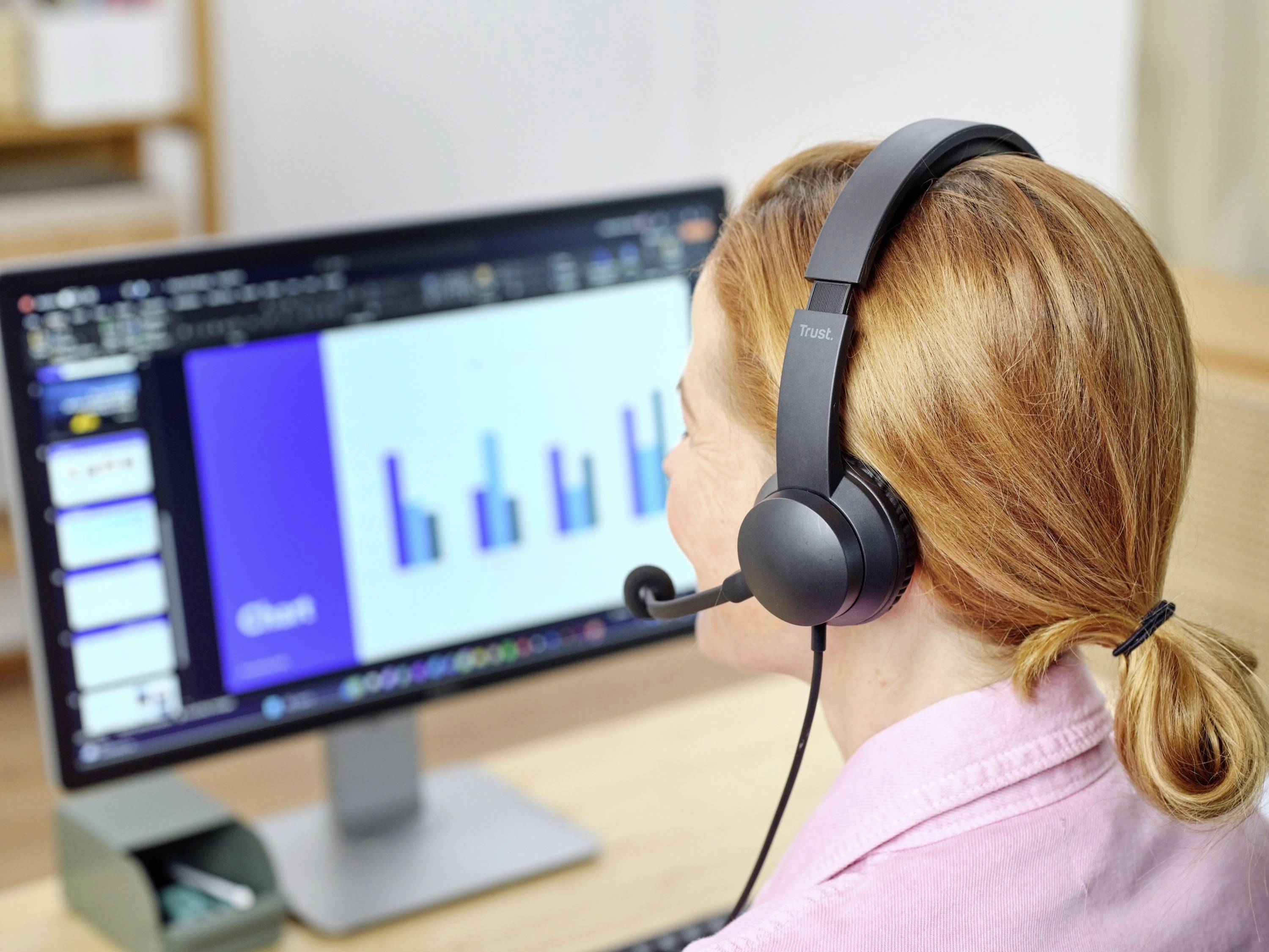 Eine Person mit Headset betrachtet ein Balkendiagramm auf einem Computermonitor, das vermutlich eine Präsentation oder Statistik zeigt.