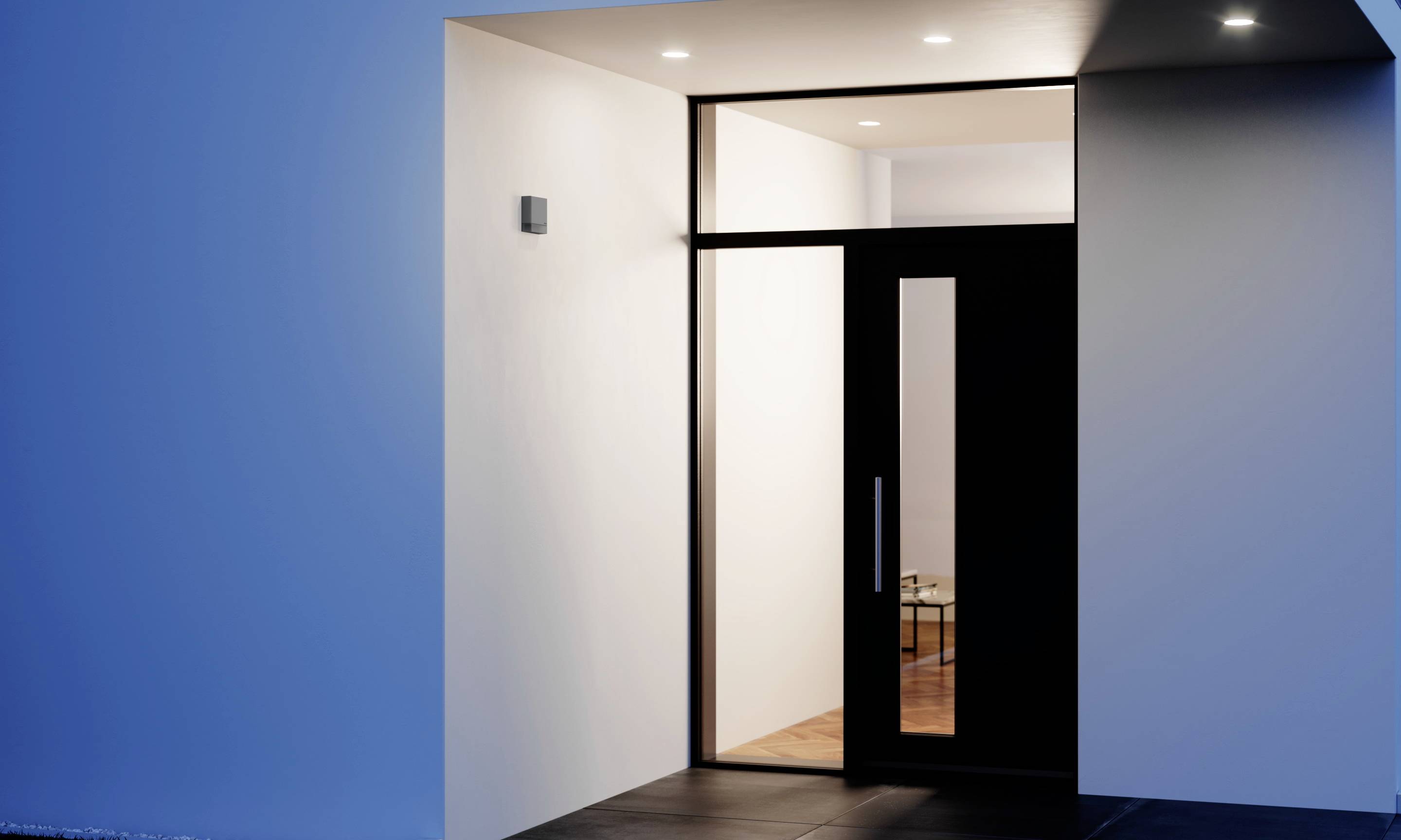 Eingang eines modernen Hauses mit Glas- und Holztür, beleuchtet von Deckenleuchten, Innenansicht eines kleinen Tisches sichtbar.