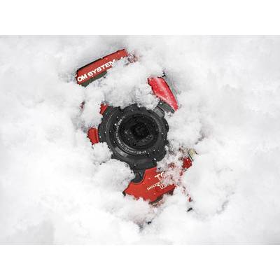 Eine rote Kamera liegt teilweise im Schnee vergraben, sichtbar ist das Objektiv. Die Umgebung ist mit weißem Schnee bedeckt.