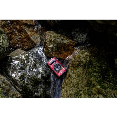 'Rote Kamera auf nassen Felsen im Bachbett; sie ist im Wasser positioniert, umgeben von moosbedeckten Steinen.'