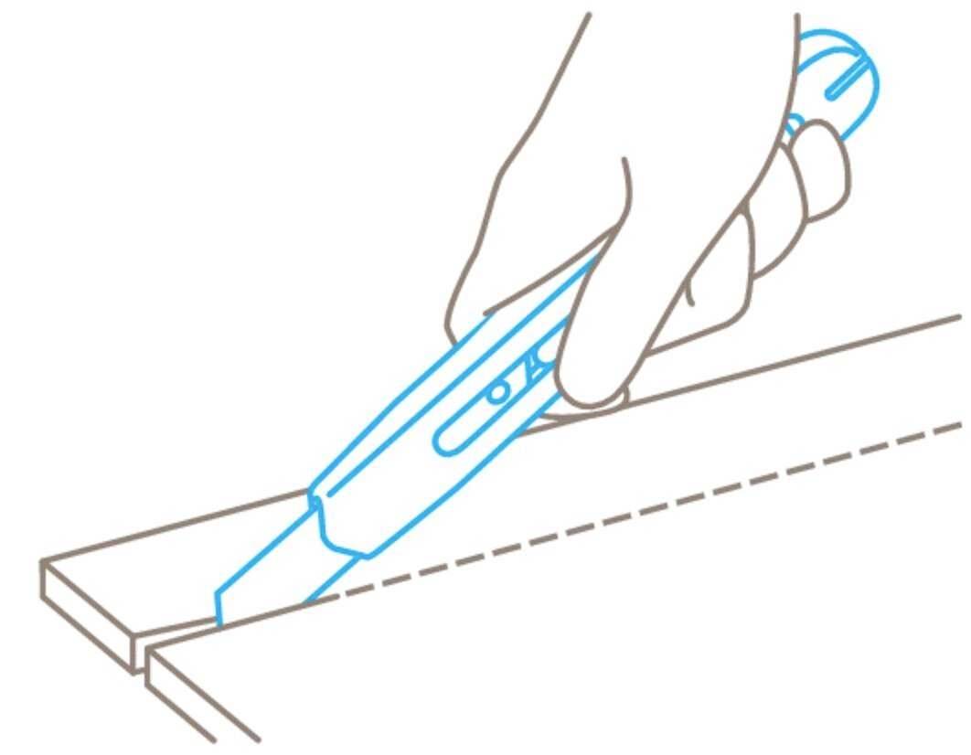 Eine Hand schneidet mit einem Teppichmesser entlang einer gestrichelten Linie auf einem Brett.