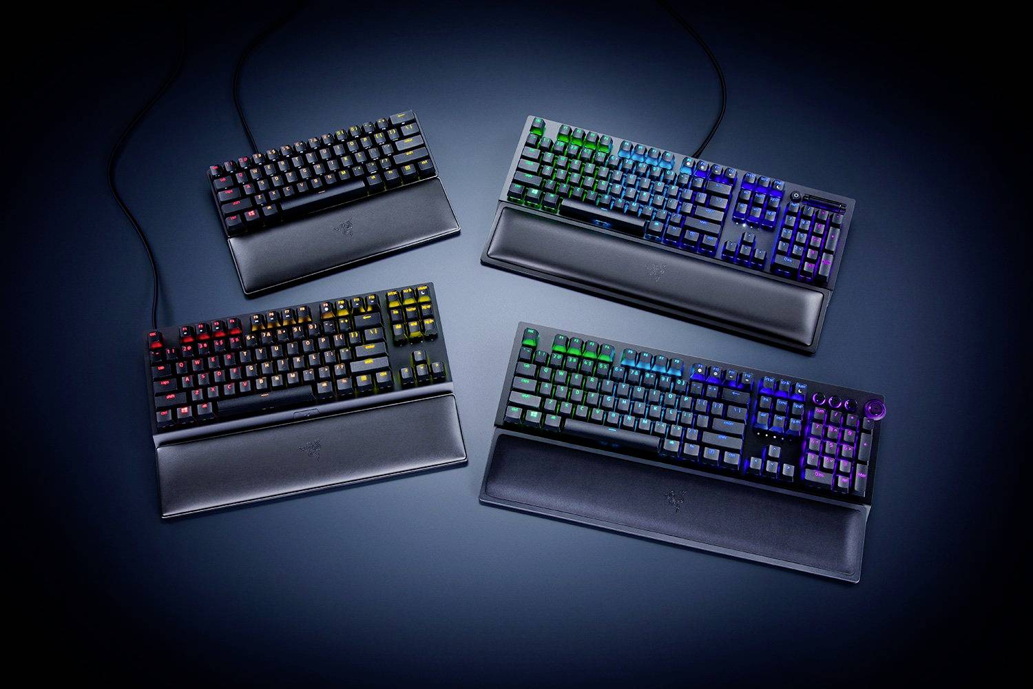 Vier Gaming-Tastaturen mit RGB-Beleuchtung in verschiedenen Farben, auf schwarzer Unterlage angeordnet.