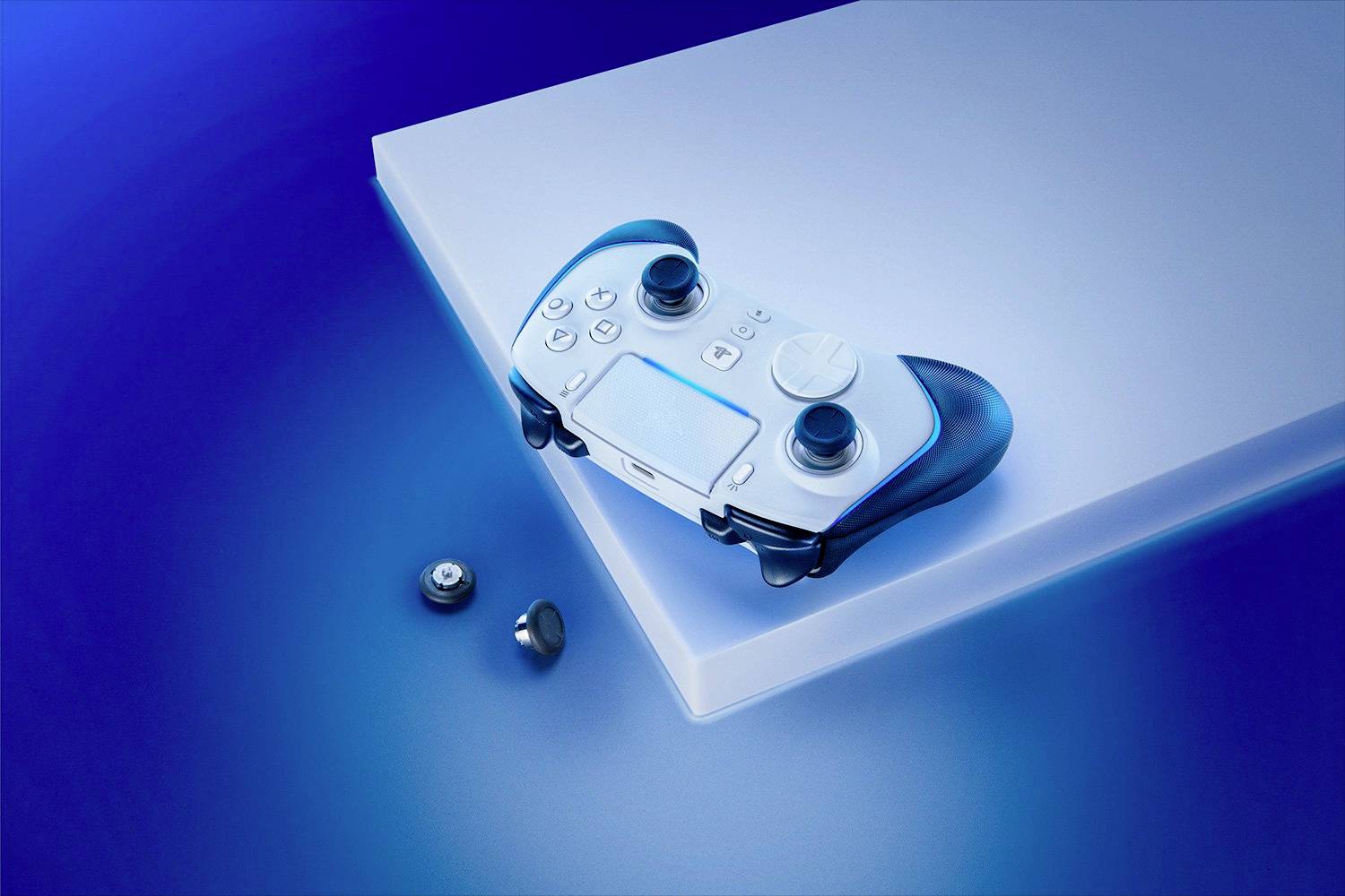 Ein weißer Gaming-Controller mit schwarzen Griffen liegt schräg auf einem Podest, daneben zwei abnehmbare Thumbsticks. Hintergrund in Blau.