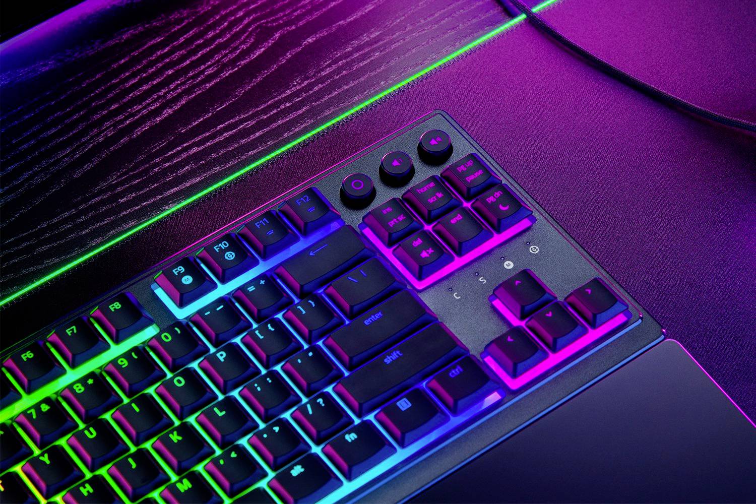 Gaming-Tastatur mit mehrfarbiger Hintergrundbeleuchtung auf einem Schreibtisch. Tastenkappen und Multimedia-Tasten sind sichtbar.