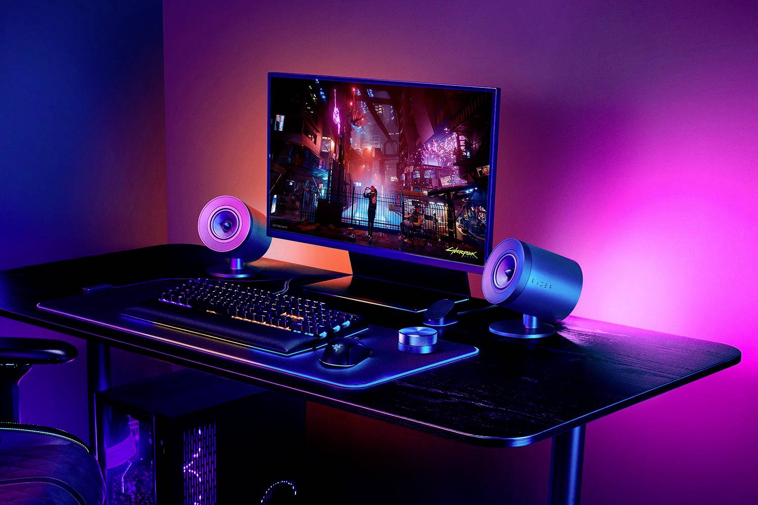 Ein Schreibtisch-Setup mit beleuchtetem Monitor, Tastatur und Lautsprechern, alles in bunter LED-Beleuchtung, das eine futuristische Atmosphäre schafft.