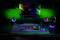 Bunt beleuchteter Schreibtisch mit Computermonitor, Tastatur, Maus, Lautsprechern und Kopfhörern. Gaming-Setup mit RGB-Lichtern.