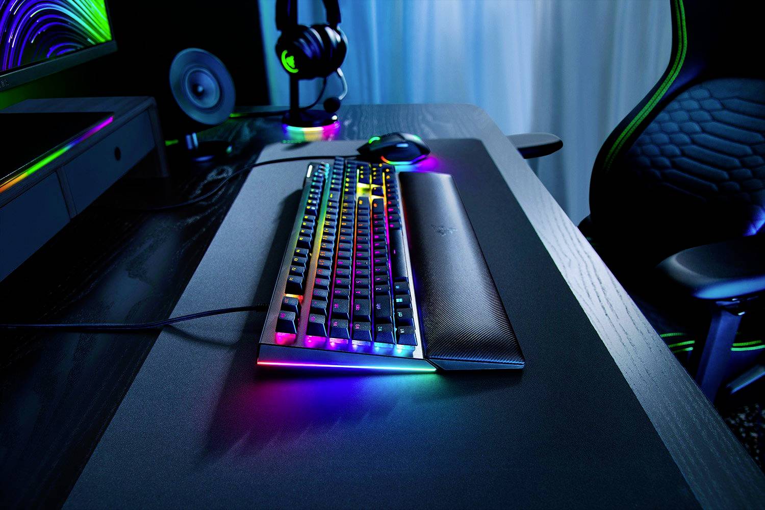 Gaming-Schreibtisch mit beleuchteter Tastatur, Maus und Gaming-Stuhl. Bunte LED-Leuchten an der Tastatur schaffen eine futuristische Atmosphäre.