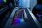Gaming-Schreibtisch mit beleuchteter Tastatur, Maus und Gaming-Stuhl. Bunte LED-Leuchten an der Tastatur schaffen eine futuristische Atmosphäre.