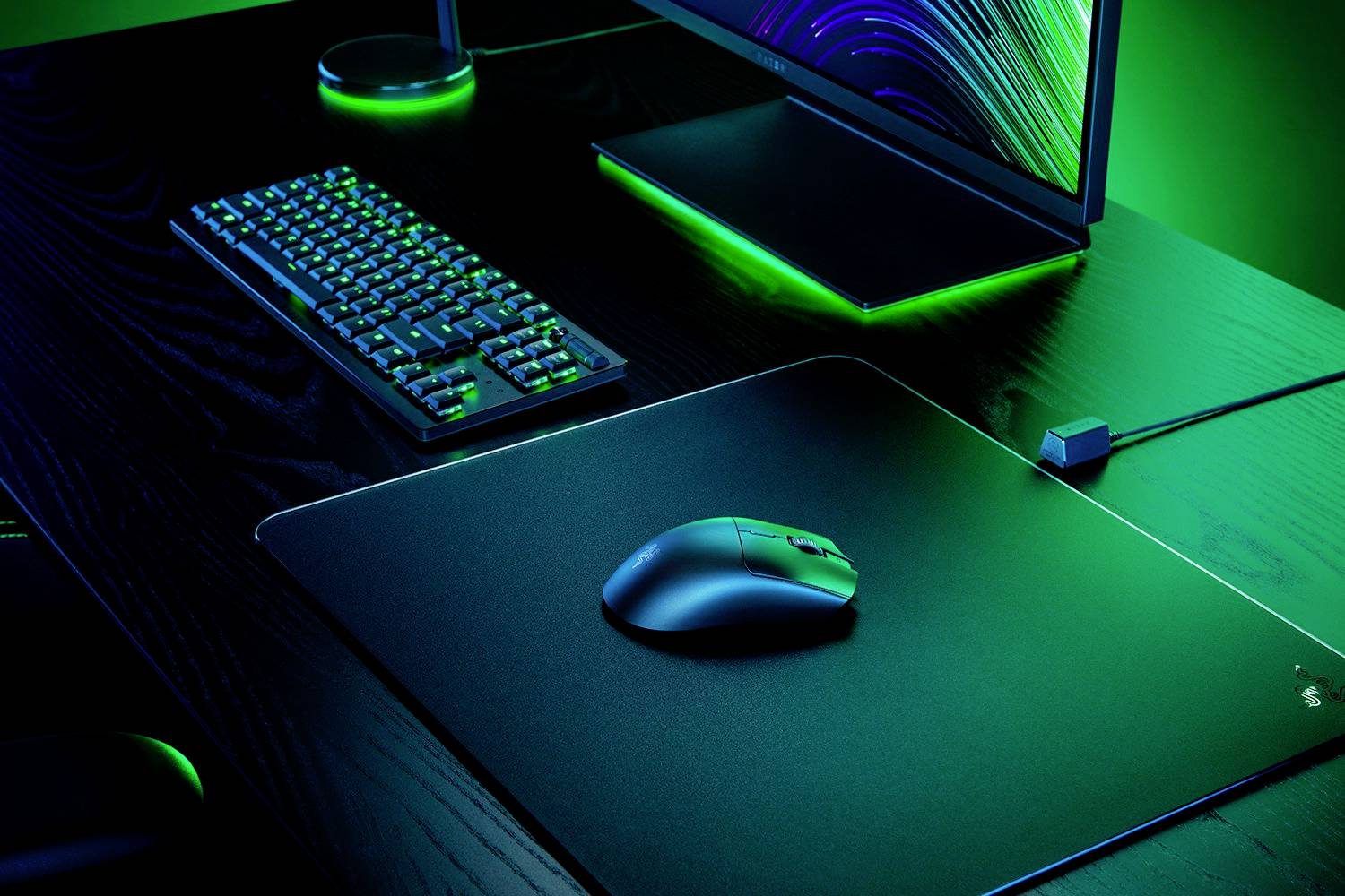 Ein moderner Computerarbeitsplatz mit beleuchtetem Gaming-Keyboard, Maus und Monitor, alles in grünem Licht auf einem dunklen Schreibtisch.