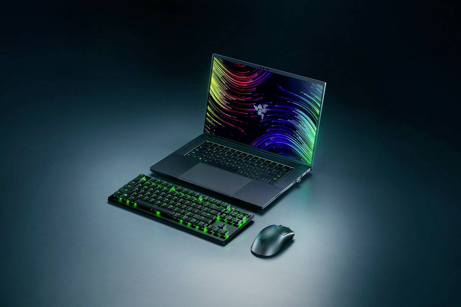 Ein geöffneter Laptop mit leuchtendem Bildschirm, daneben eine beleuchtete Tastatur und kabellose Maus auf dunkelgrauem Hintergrund.