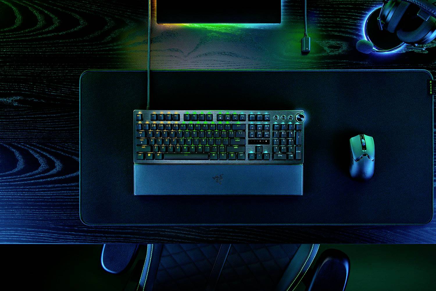 Eine beleuchtete Tastatur und Maus auf einem Schreibtisch mit dunkler Holzoberfläche. Oben rechts liegen Kopfhörer.