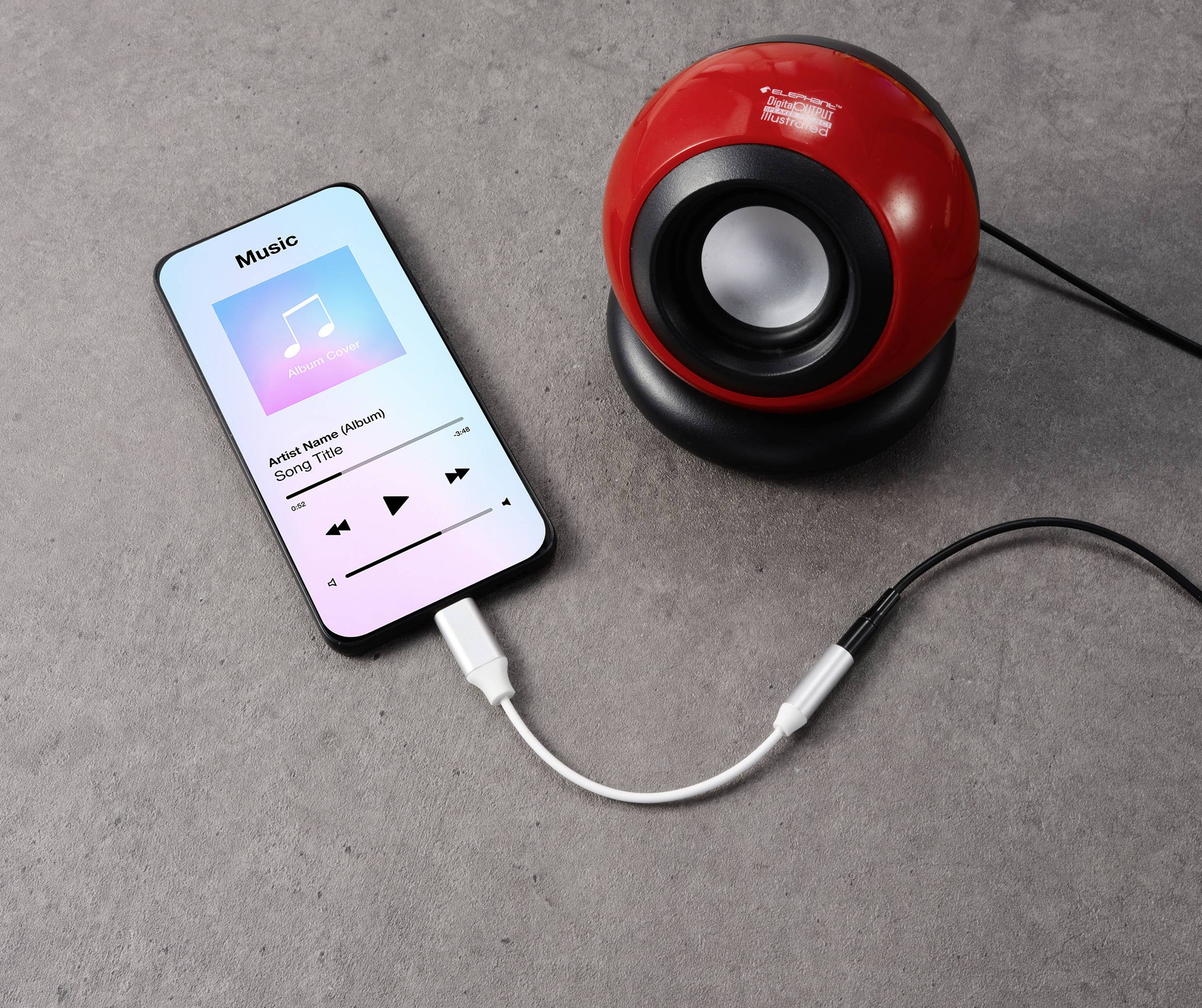 Ein Smartphone spielt ein Lied ab und ist über ein Kabel mit einem roten, kugelförmigen Lautsprecher verbunden.