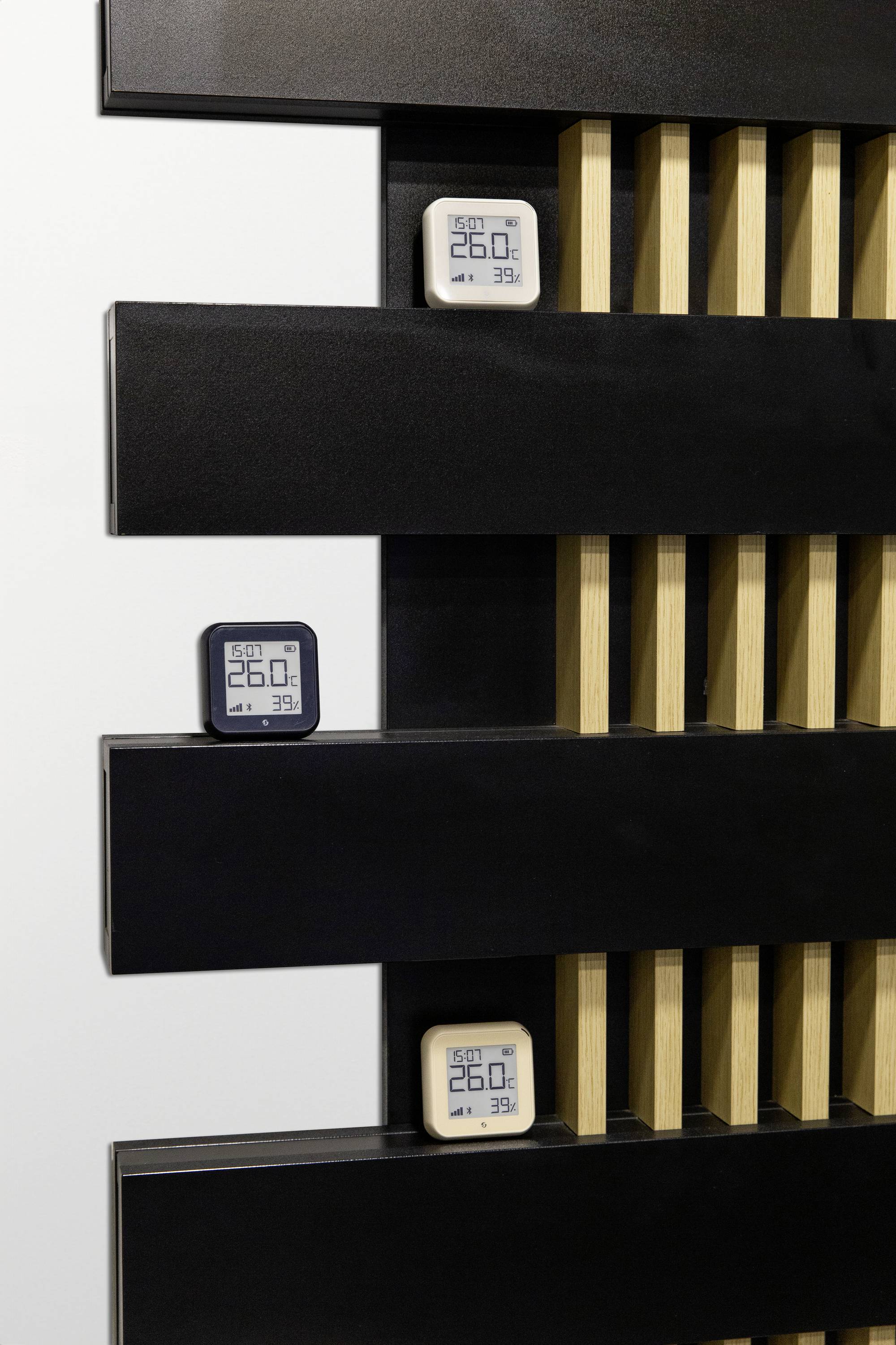 Drei digitale Thermometer und Hygrometer sind auf einer modernen schwarzen und holzfarbenen Wand befestigt. Sie zeigen 26,0°C und 39% Luftfeuchtigkeit an.