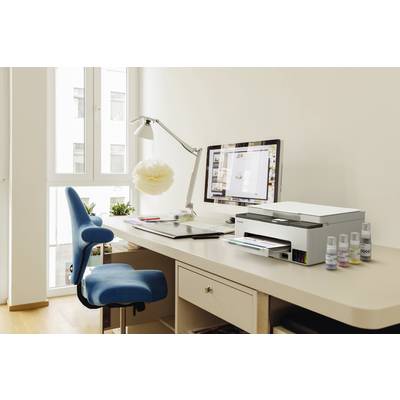 Arbeitsplatz mit einem Computer, Drucker und blauer Bürostuhl auf einem hellen Holztisch, umgeben von Fenstern mit Tageslicht.