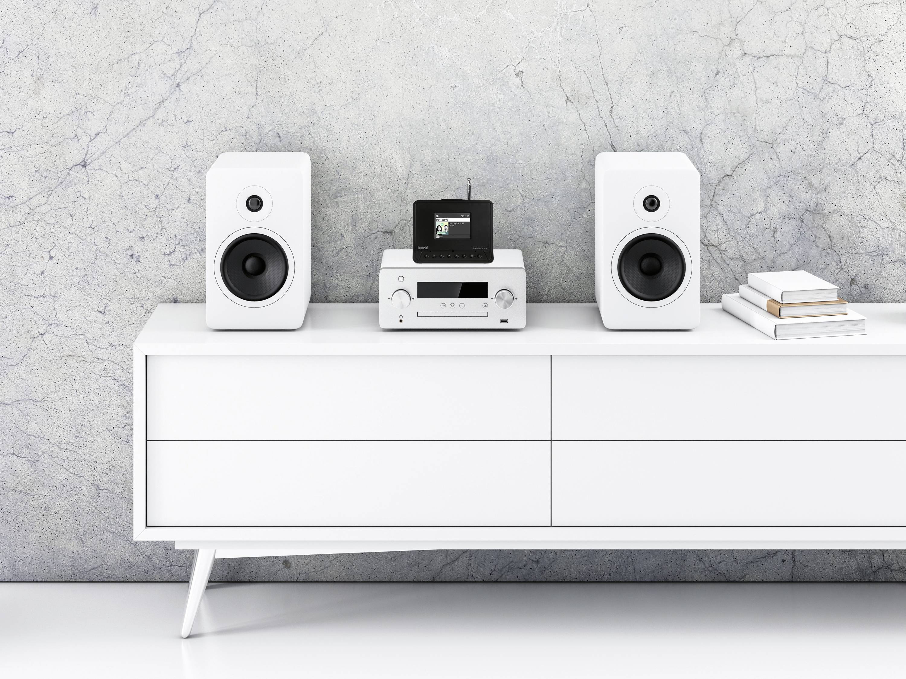 Weiße Kommode mit zwei Lautsprechern, einem Stereo-Verstärker und kleinen gestapelten Büchern in einem modernen Wohnraum.