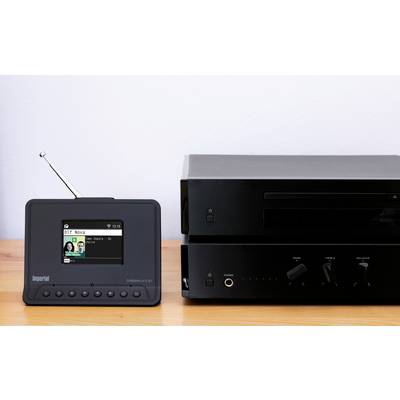 Kompakte schwarze Digitalradio-Anlage neben einem Verstärker auf einem Holzregal. Die Geräte haben Knöpfe und eine Antenne.