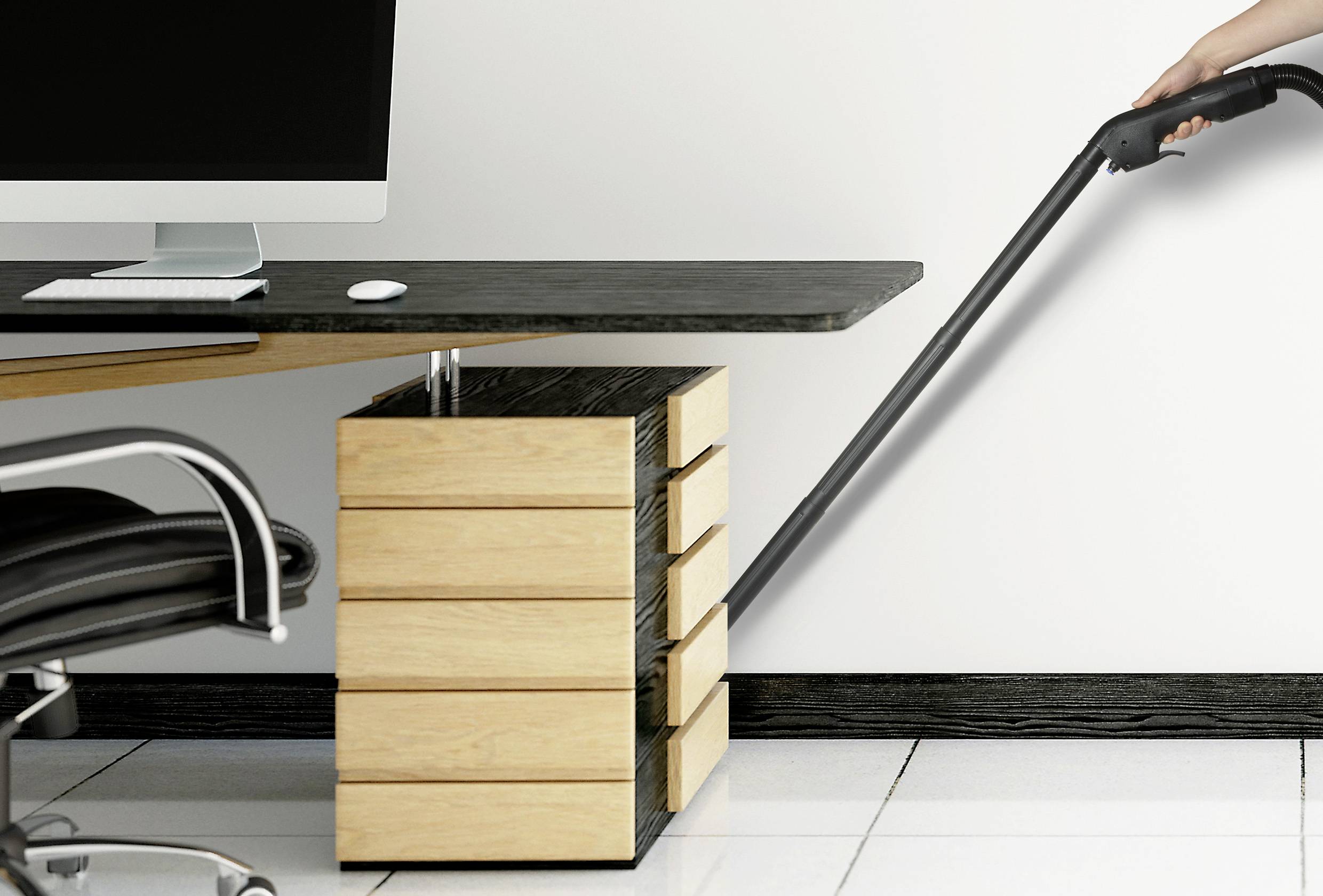 Eine Person staubsaugt den Boden eines modernen Büroraums. Im Vordergrund ein Schreibtisch mit Computer und kleiner Schubladenschrank.