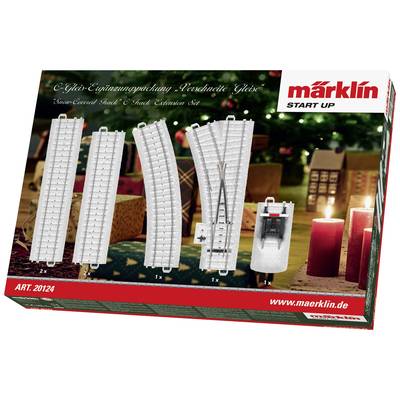 Eine Weihnachtsverpackung von Märklin mit Schienen und Zubehör. Im Hintergrund sind Kerzen und ein geschmückter Baum.