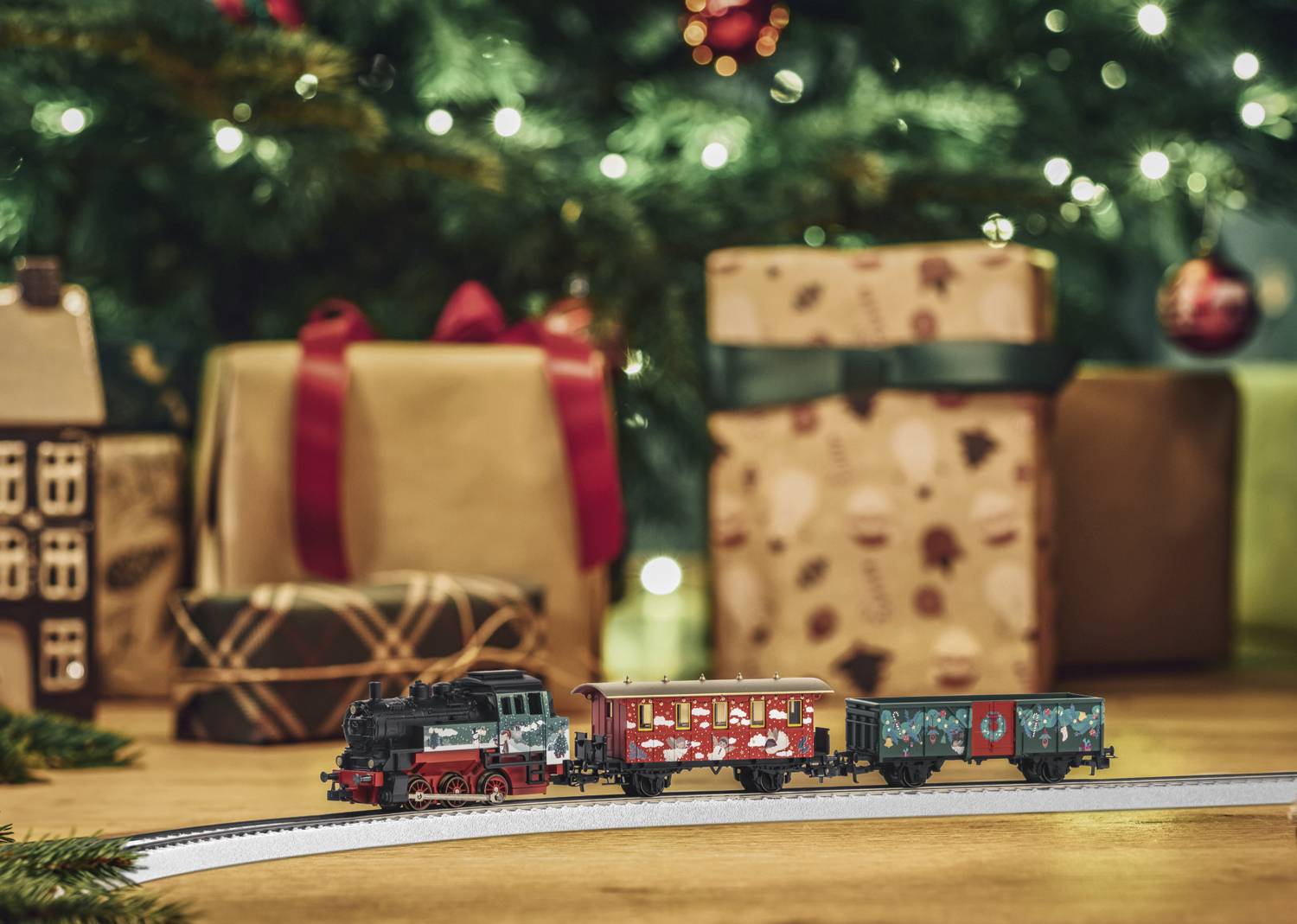 Eine Spielzeugeisenbahn fährt vor einem geschmückten Weihnachtsbaum. Im Hintergrund sind Geschenke mit Schleifen zu sehen.