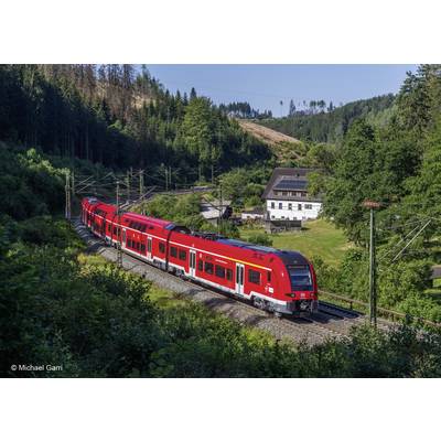 'Ein roter Regionalzug fährt tagsüber durch eine waldige Landschaft. Im Hintergrund ist ein weißes Gebäude zu sehen.'