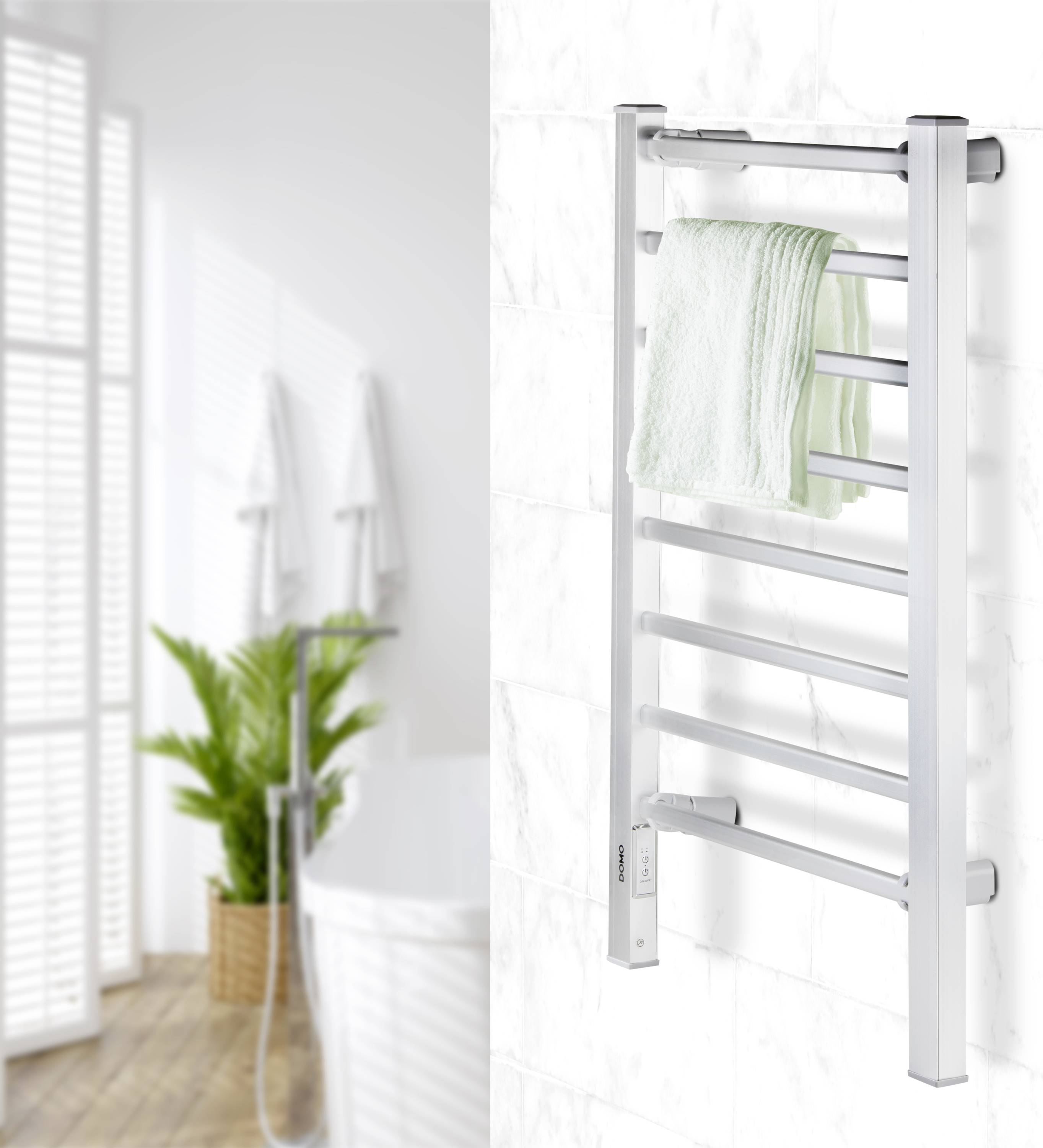 Ein Handtuchhalter im Badezimmer, an dem ein grünes Handtuch hängt. Im Hintergrund sind Pflanzen und eine Duscharmatur zu sehen.