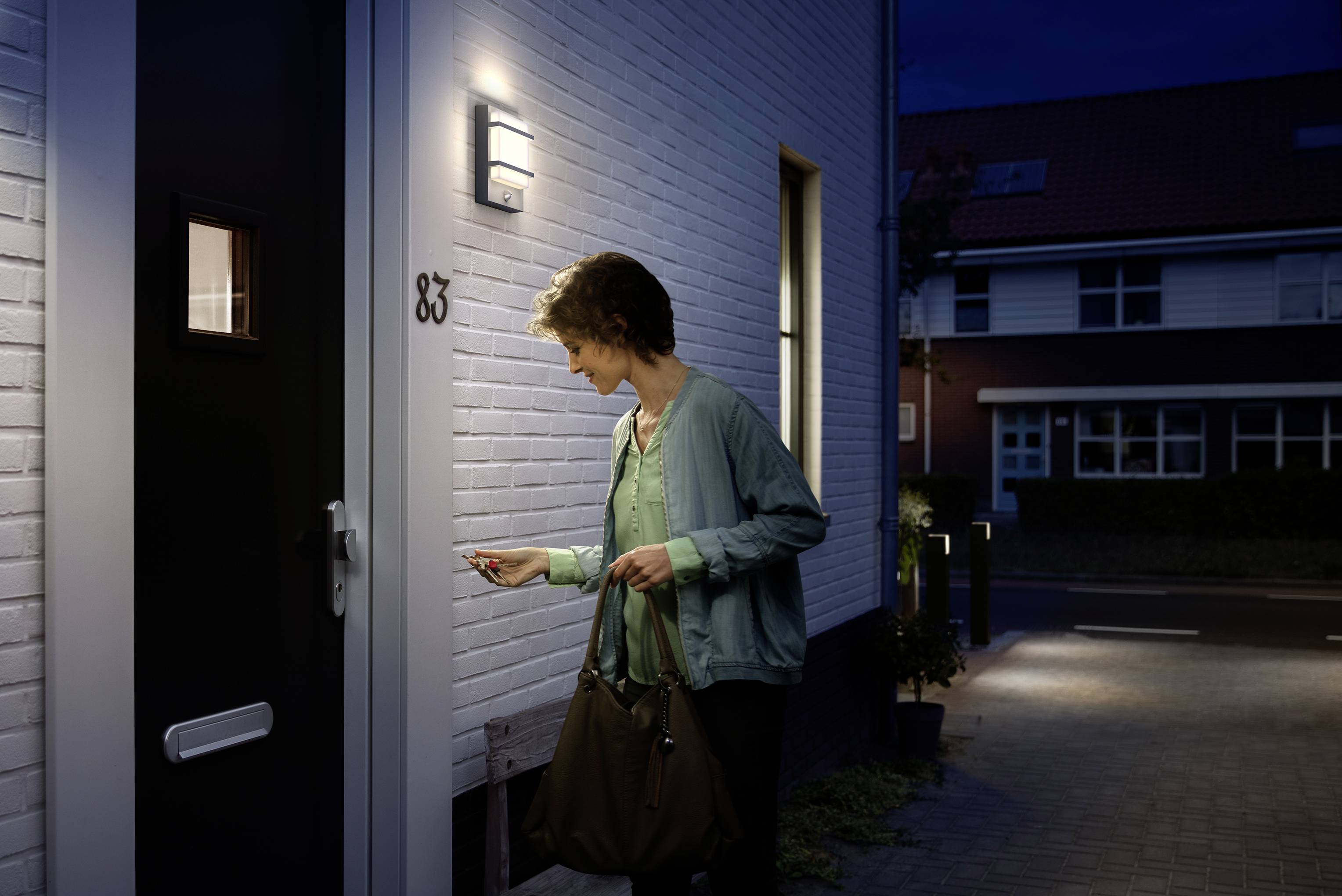 Eine Person steht vor einer Haustür und benutzt eine Schlüsselkarte, um einzutreten. Es ist Nacht, das Licht der Lampe leuchtet.