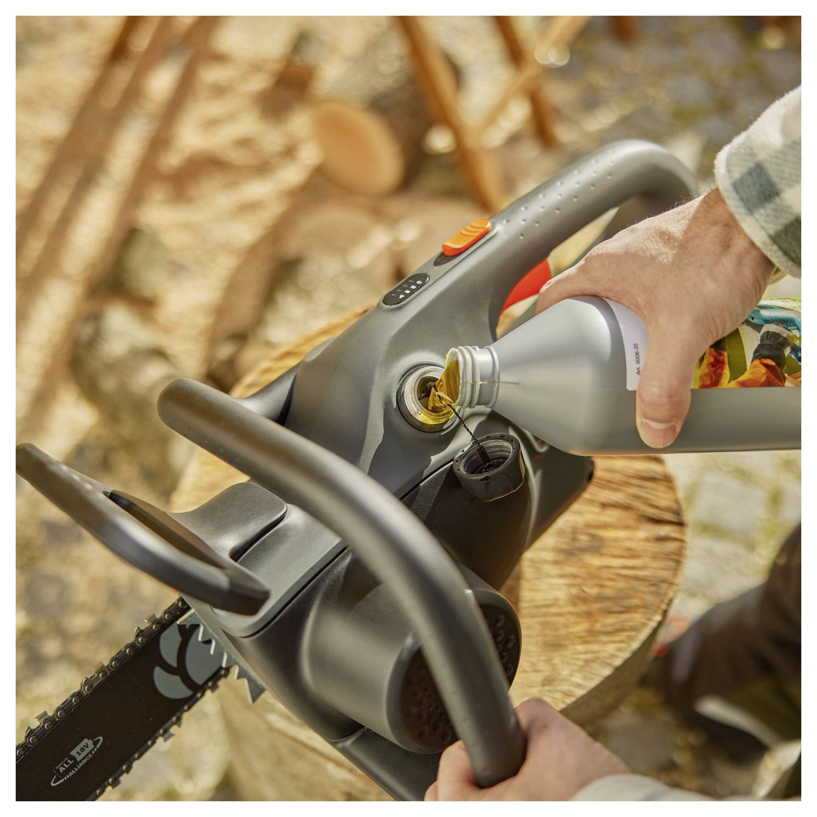 Eine Person gießt Kettensägenöl in eine Kettensäge auf einer Holzoberfläche im Freien, was Wartung oder Vorbereitung zur Nutzung andeutet.