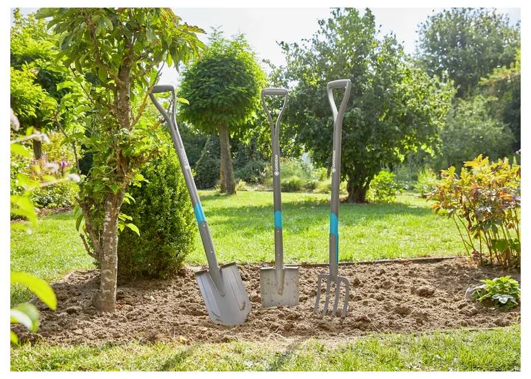 Drei Gartengeräte mit blauen Griffen, darunter eine Schaufel, eine Spaten und eine Gabel, die aufrecht in einem frisch bearbeiteten Gartenbereich stehen.