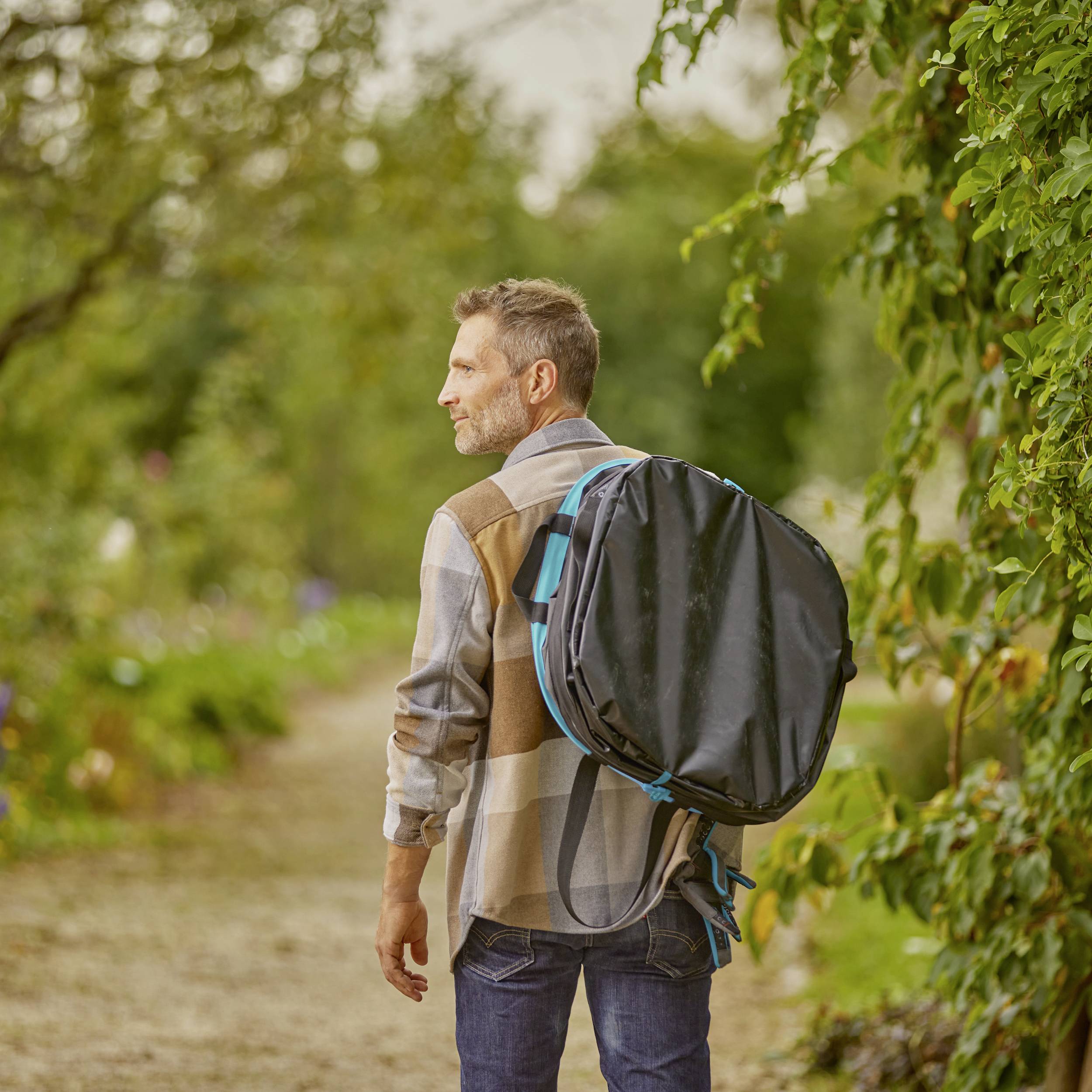 Mann mit Rucksack geht auf einem Waldweg. Bäume und Pflanzen umgeben den Pfad. Es ist ein entspannter Spaziergang in der Natur.