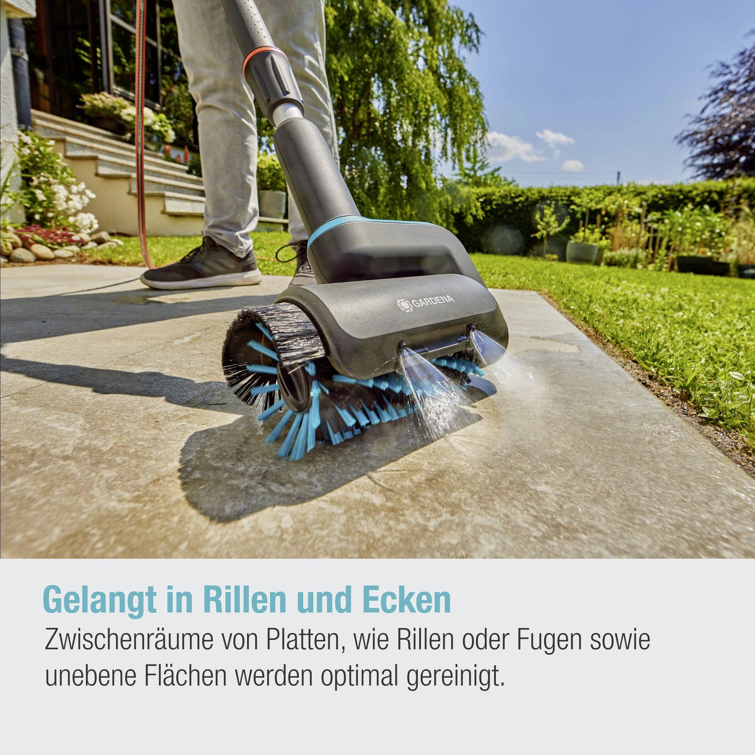 Ein Gerät reinigt Fugen auf einer Terrassenfläche. Text: 'Gelangt in Rillen und Ecken'. Hintergrund zeigt Pflanzen und einen sonnigen Tag.