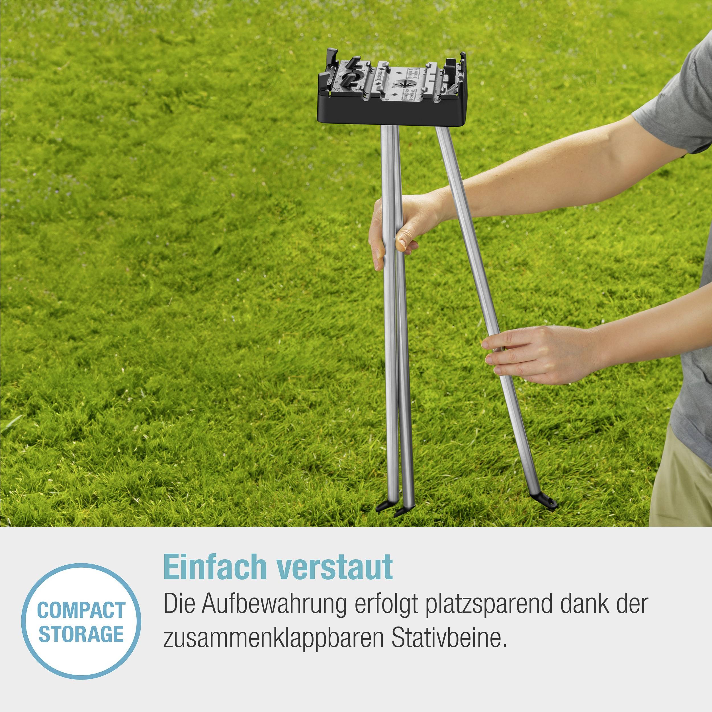 Kompakter Grill auf klappbarem Stativ in grünem Garten. Text: 'Einfach verstaut dank klappbarer Stativbeine.'