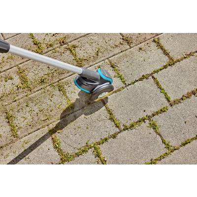 Ein Gartenwerkzeug entfernt Moos und Unkraut aus den Zwischenräumen von Pflastersteinen auf einem Gehweg.