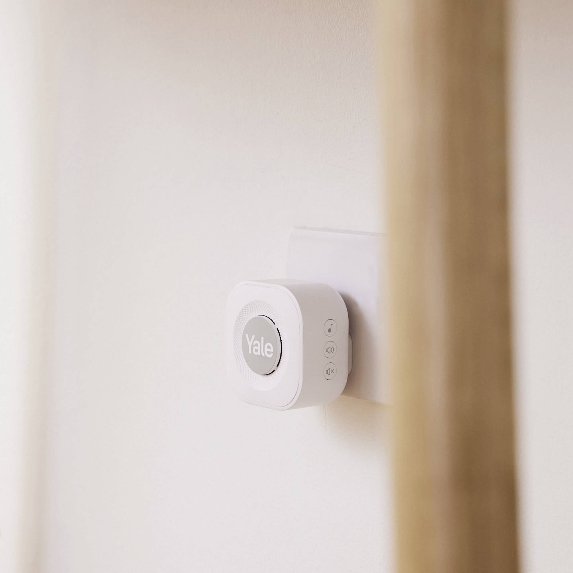 Kleiner, an der Wand montierter, weißer Yale-Sensor mit Logo. An einer Holzstange im Vordergrund befestigt.