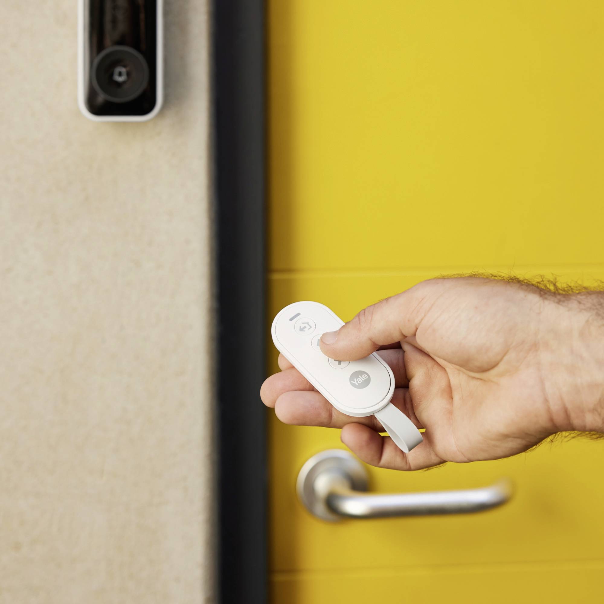 Eine Hand hält ein Gerät zur Türöffnung vor einer gelben Tür mit smartem Türspion; Symbol für moderne Zugangstechnologie.