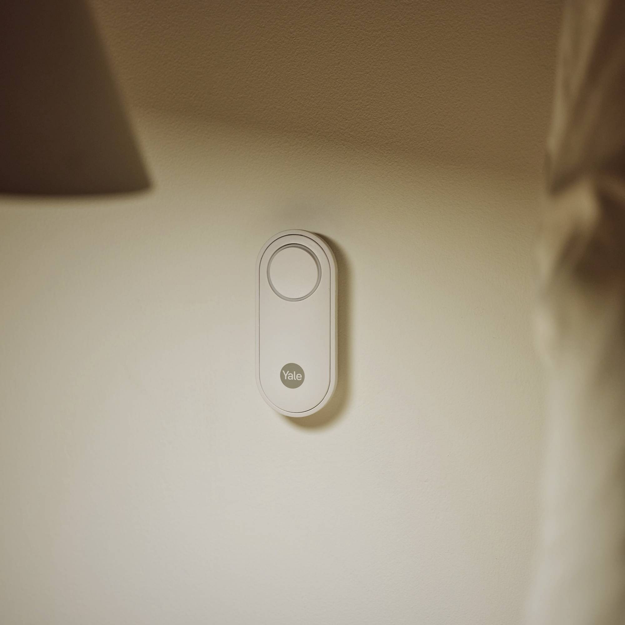 Eine smarte Türklingel ist an einer hellen Wand angebracht. Sie hat ein modernes, minimalistisches Design mit einem kreisförmigen Knopf.