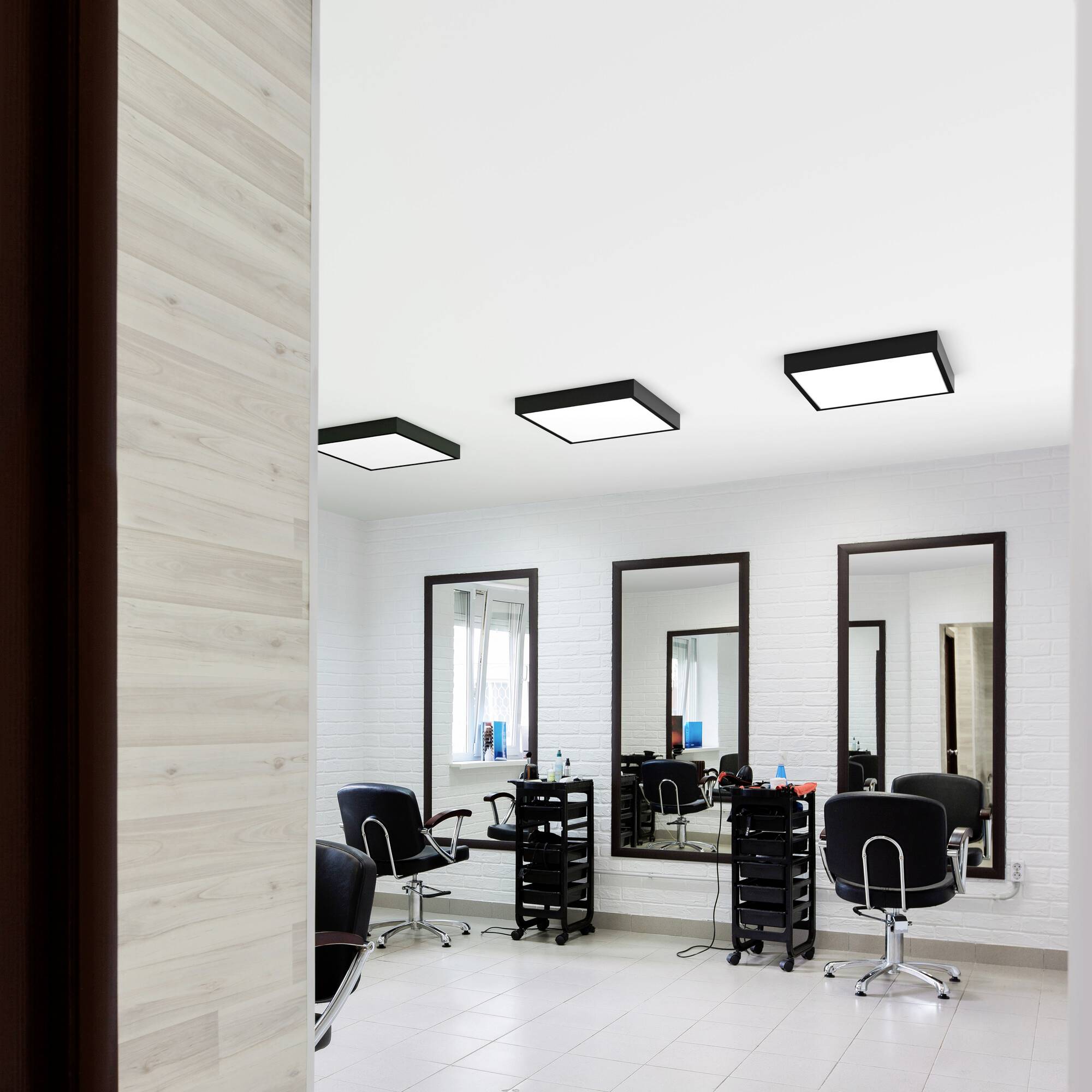 Friseursalon mit leeren Stühlen vor großen Spiegeln und hellem, modernem Design.