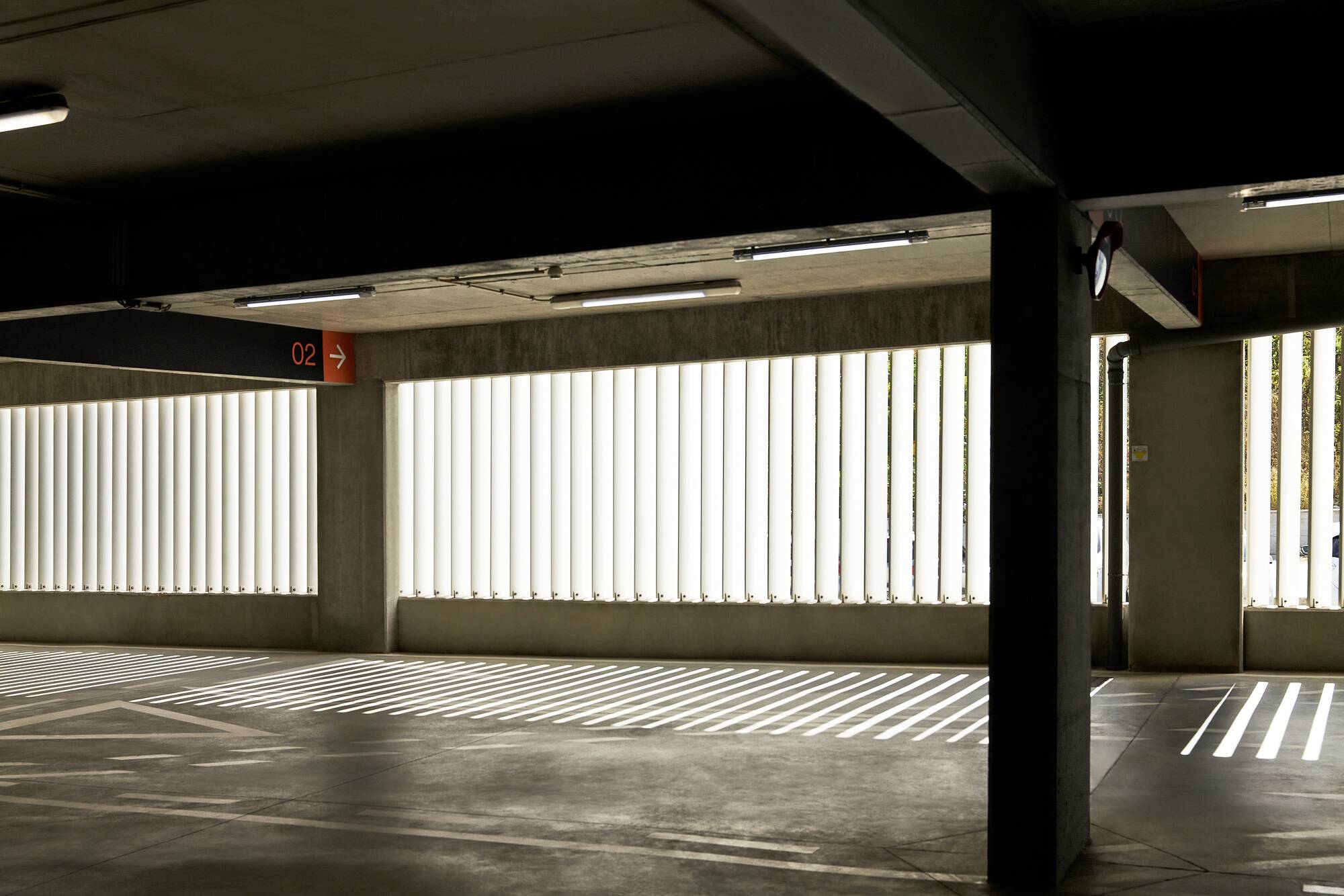 Leerer, gut beleuchteter Parkhausbereich mit Schattenlinie auf dem Boden, vertikalen Fenstergittern und Beschilderung 'C2'.