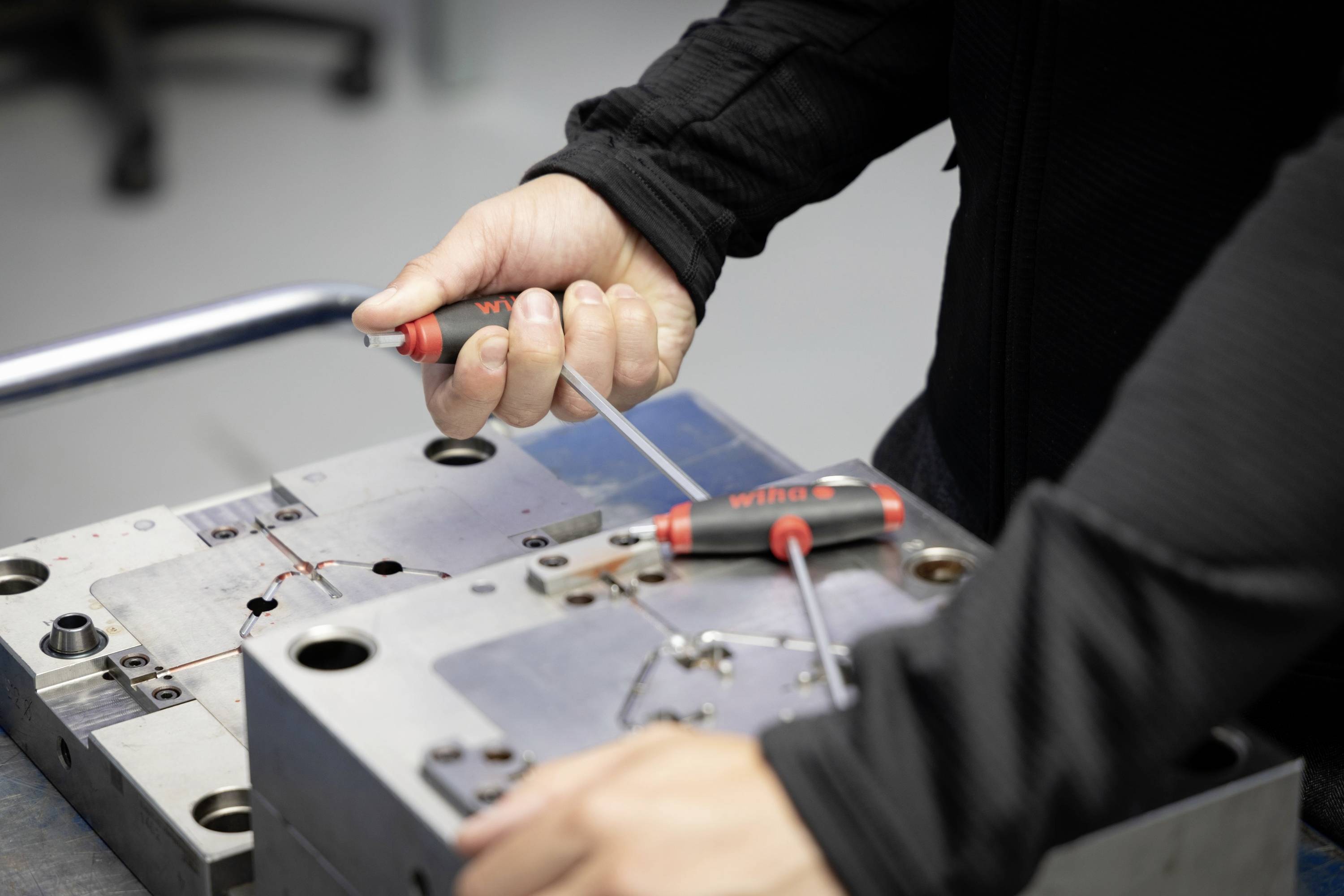 Eine Person arbeitet mit Schraubendrehern an einem Metallblock in einer Werkstattumgebung, vermutlich bei der Montage oder Reparatur.