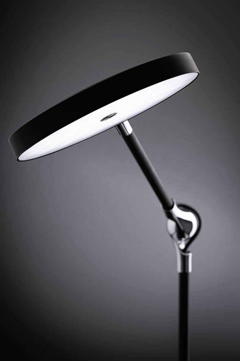 Schwarze Stehlampe mit rundem flachem Kopf und verstellbarem Arm in modernem Design, erleuchtet den Raum gleichmäßig.