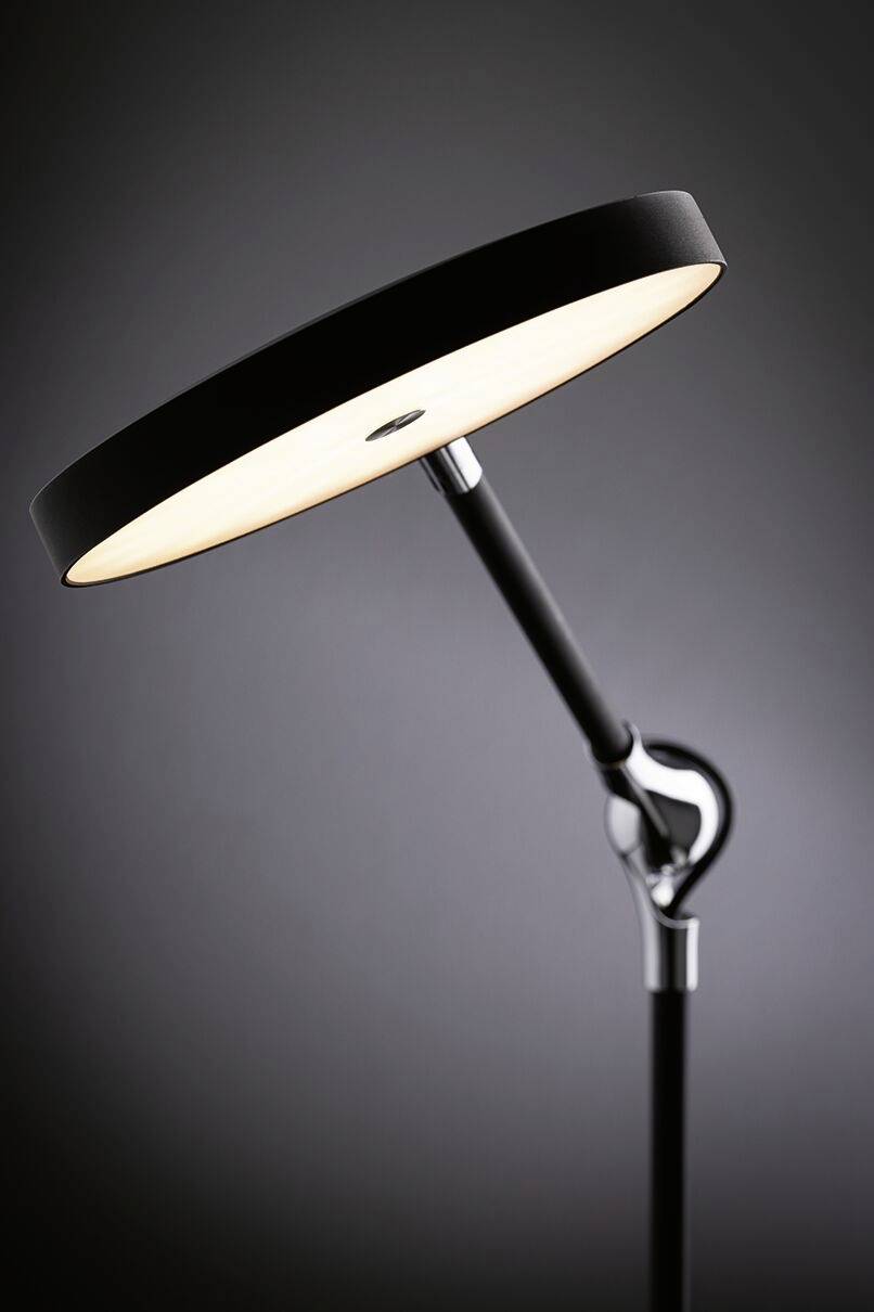 Eine moderne Stehlampe mit einem flachen, runden Lampenschirm leuchtet in einem dunklen Raum. Ihr schlichtes Design wirkt elegant und funktional.