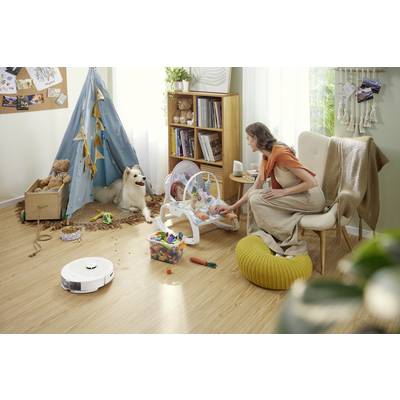 Eine Frau kümmert sich liebevoll um ein Baby in einer Schaukel im Kinderzimmer. Ein Hund sitzt neben einem Zelt voller Spielzeuge.