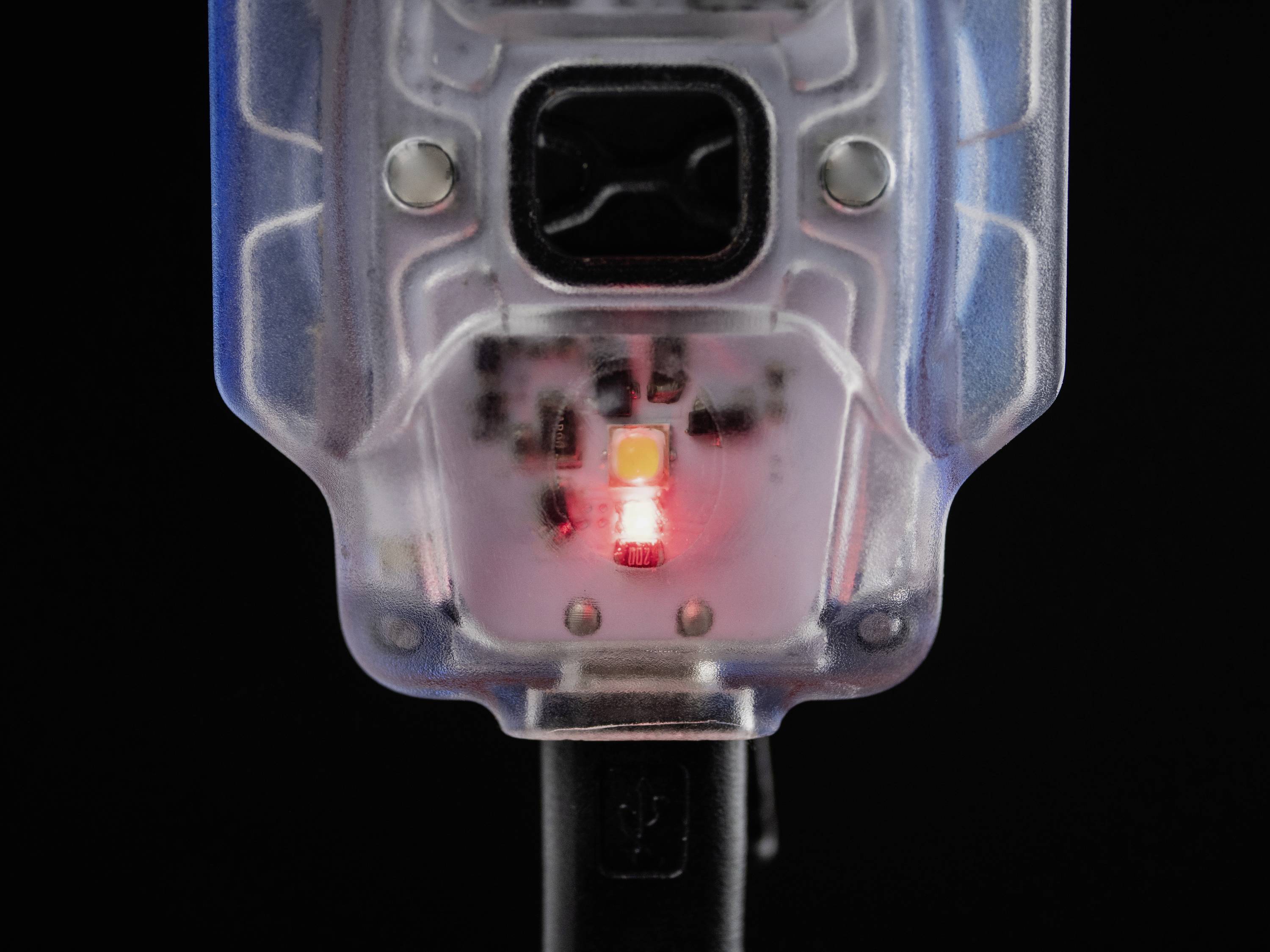 Ein durchsichtiger Plastikstecker mit einer leuchtenden roten LED in der Mitte, deutet auf Aktivität oder Ladestatus hin.