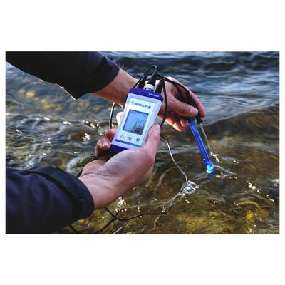 Eine Person, die ein digitales Gerät verwendet, um die Wasserqualität in einem Fluss zu messen, wobei eine Ablesung von 7,4 angezeigt wird.