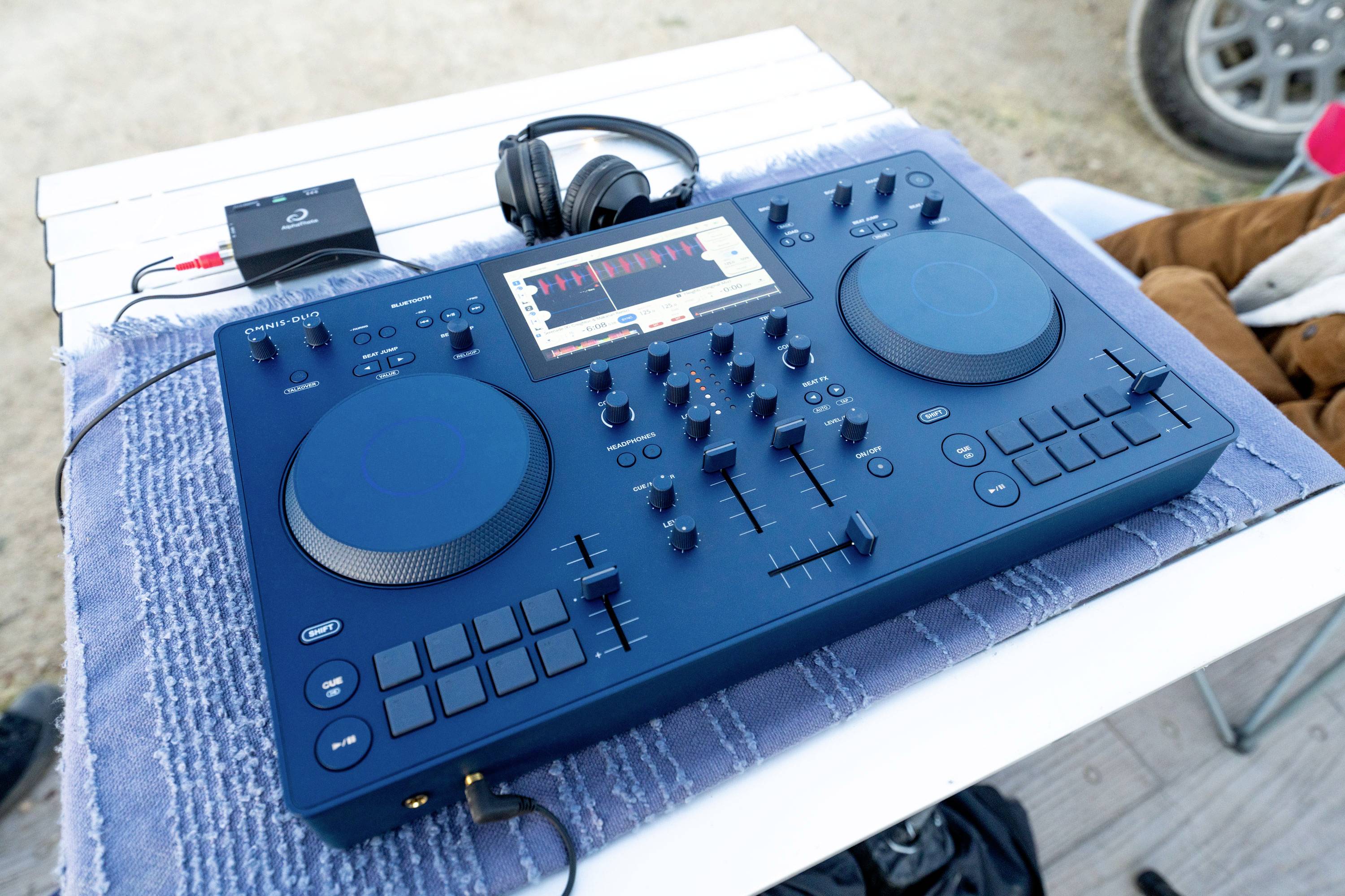 Ein blauer DJ-Controller auf einem Tisch mit Kopfhörern. Das Display zeigt Musikbearbeitungssoftware.