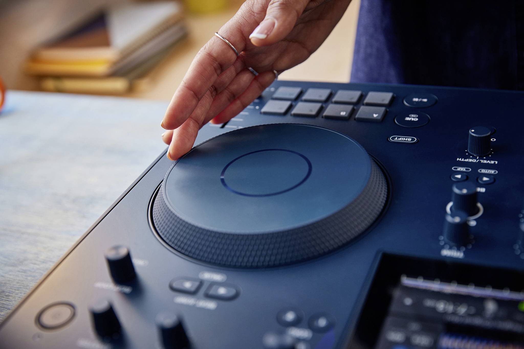 Eine Hand bedient ein DJ-Set mit einem großen runden Plattenteller und mehreren Tasten, die auf einer Konsole angeordnet sind.