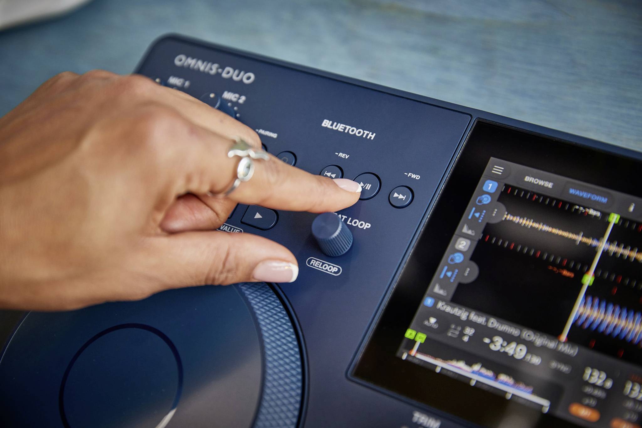 Nahaufnahme einer Hand, die die Steuertasten eines Audiosystems mit Display drückt, auf dem Musikgrafiken und Bluetooth angezeigt werden.