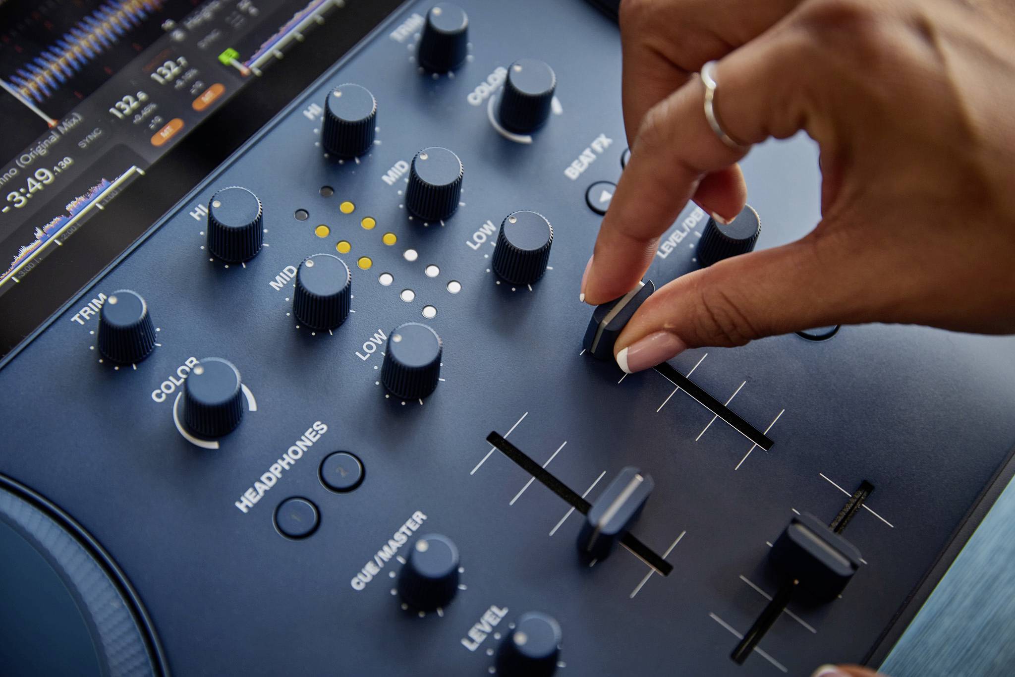 Eine Hand justiert einen Regler auf einem Audiomischpult mit mehreren Drehknöpfen und Schiebereglern, verwendet für Tonanpassungen.