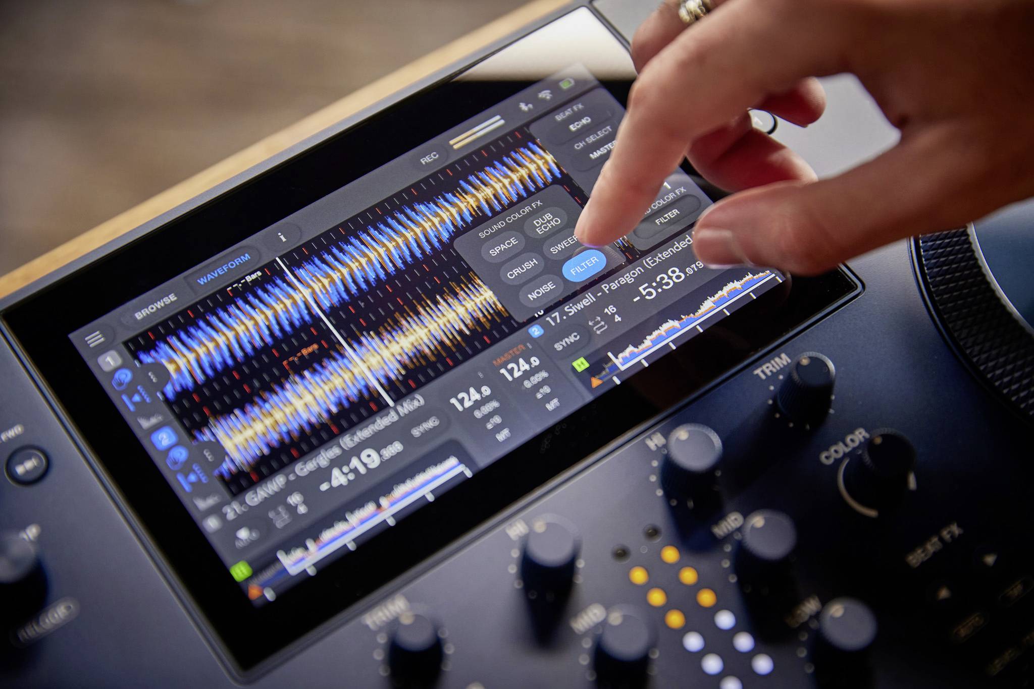 Eine Hand bedient ein Touchscreen-Audiointerface mit verschiedenen Reglern und Anzeigen für Musikbearbeitung und -steuerung.