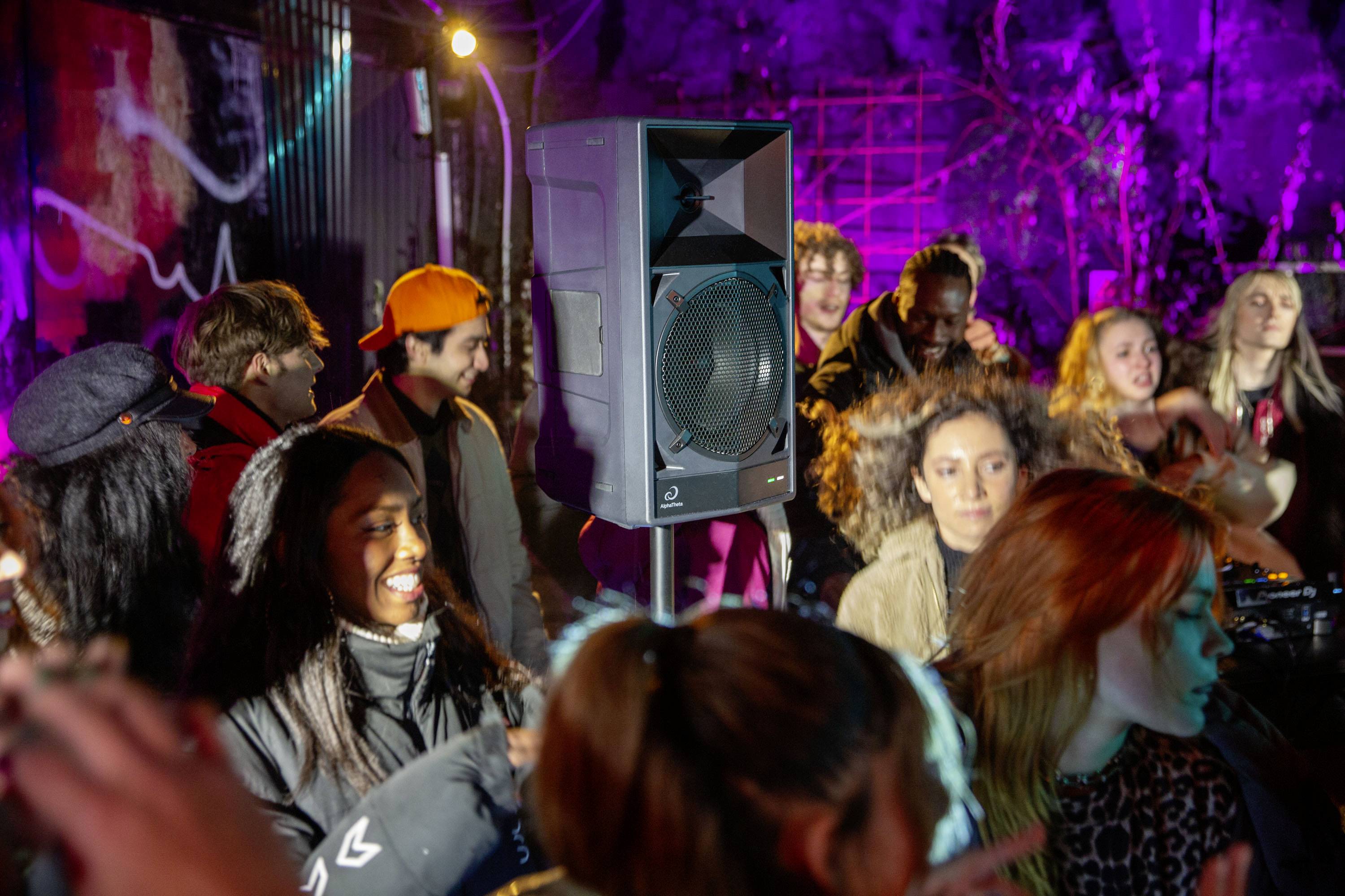 Eine Gruppe von Menschen feiert ausgelassen in einem Club bei buntem Licht. Sie tanzen und lachen, während Musik im Hintergrund spielt.
